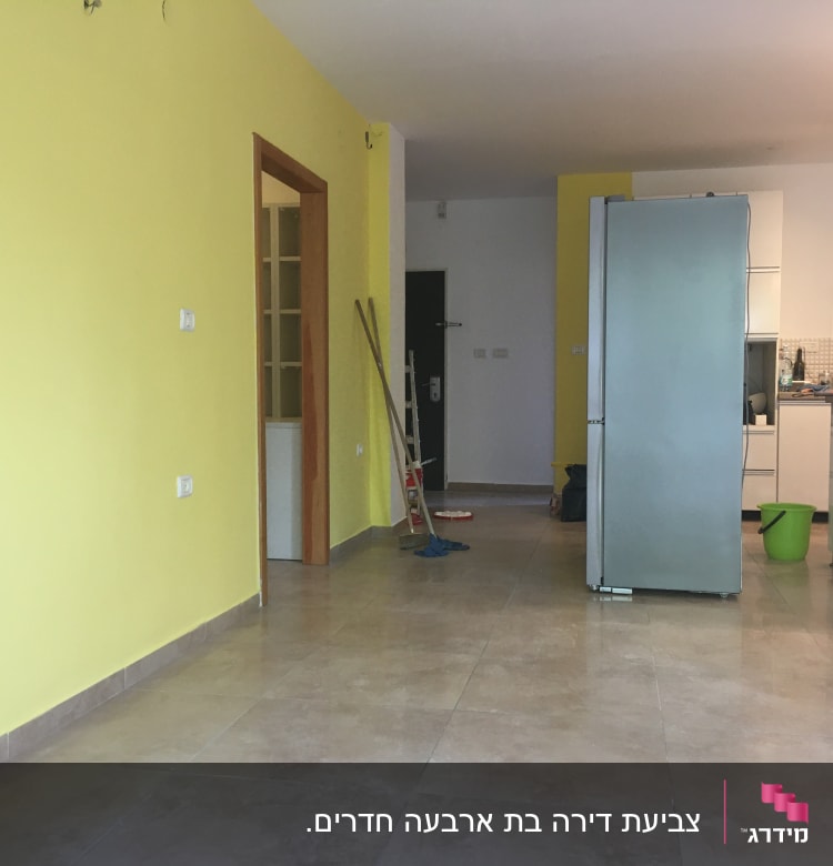 קיר צבוע בצהוב עם כלי צביעה על הרצפה